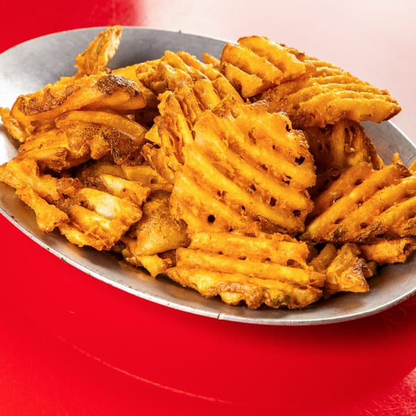 A metal platter overflowing with golden-brown, crispy waffle fries on a vibrant red surface.