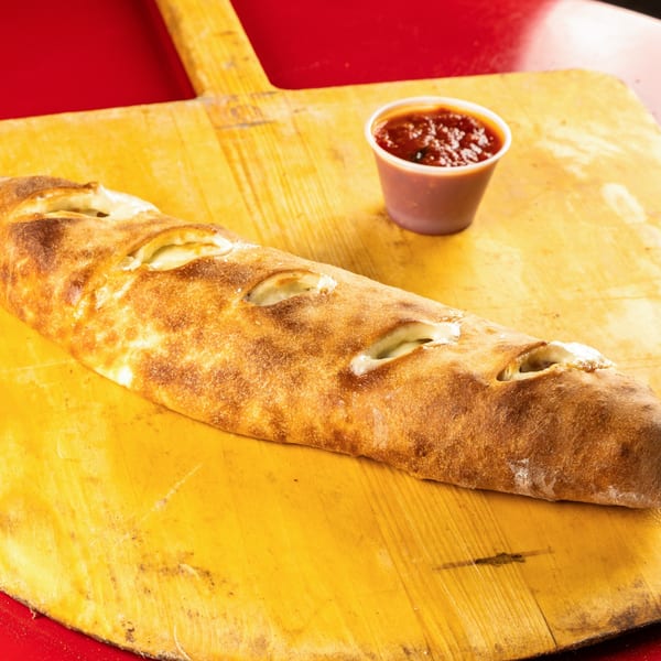 A golden-brown calzone with visible cheese filling, served with a side of marinara sauce on a pizza peel.